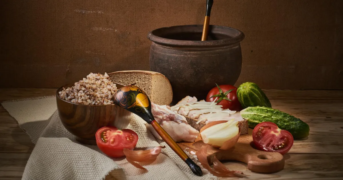 Cozy rustic still life featuring buckwheat, vegetables, and traditional tableware on a wooden surface.