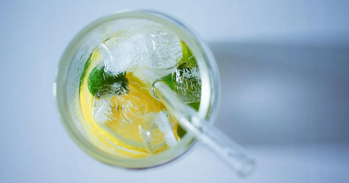 Top view of a refreshing cold drink with lemon, lime, and ice cubes in a clear glass.