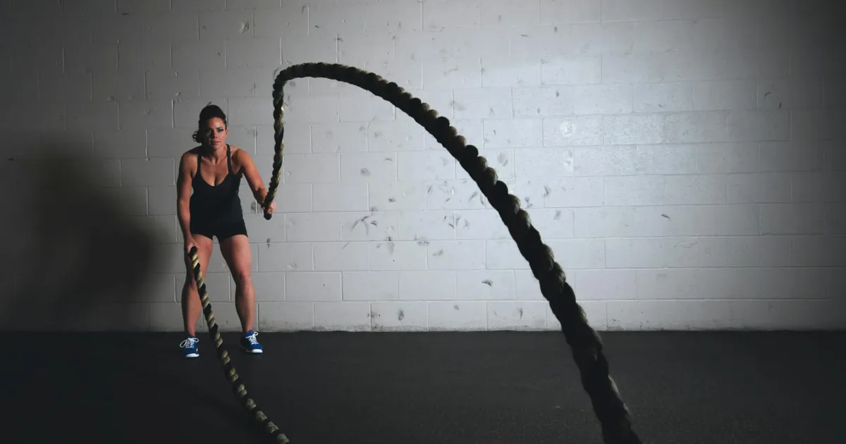 A focused woman performs a dynamic battle rope exercise in a gym setting, demonstrating strength and fitness.
