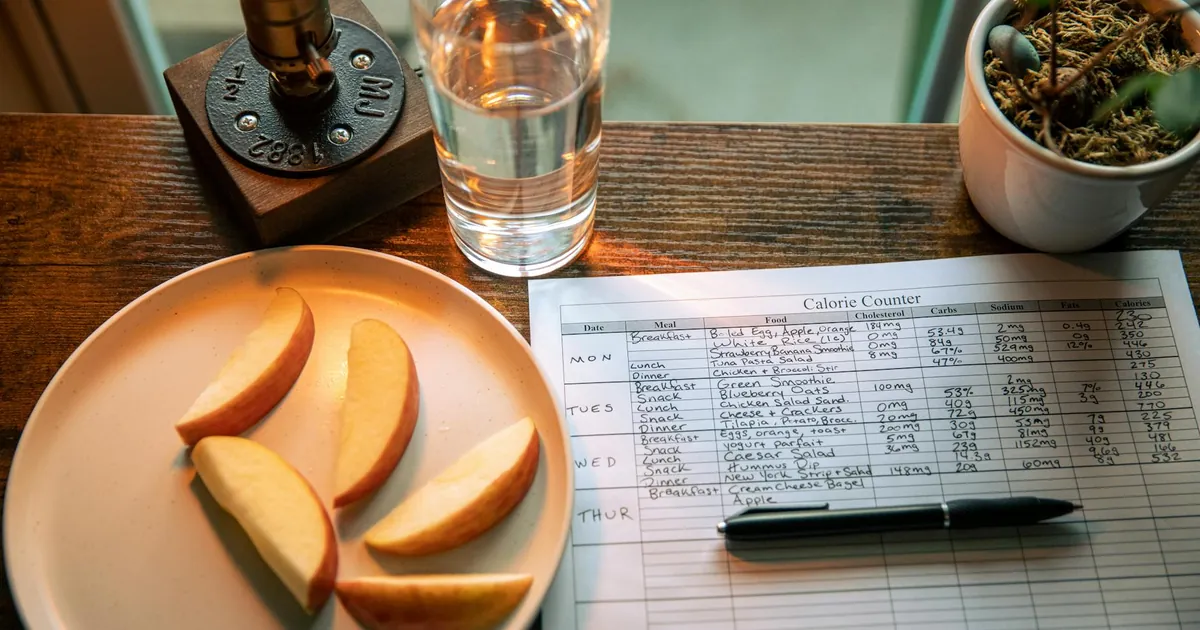 A wooden table setup with apple slices, a calorie chart, and a glass of water for a healthy diet plan.
