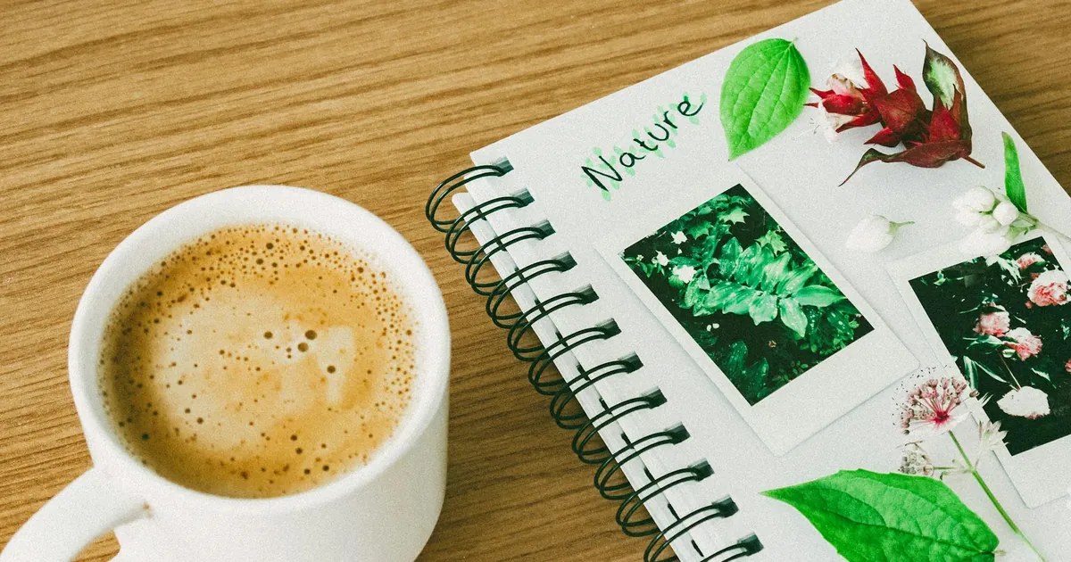 A calming still life image featuring a coffee cup and a nature-themed notebook on a wooden table. A calming still life image featuring a coffee cup and a nature-themed notebook on a wooden table.