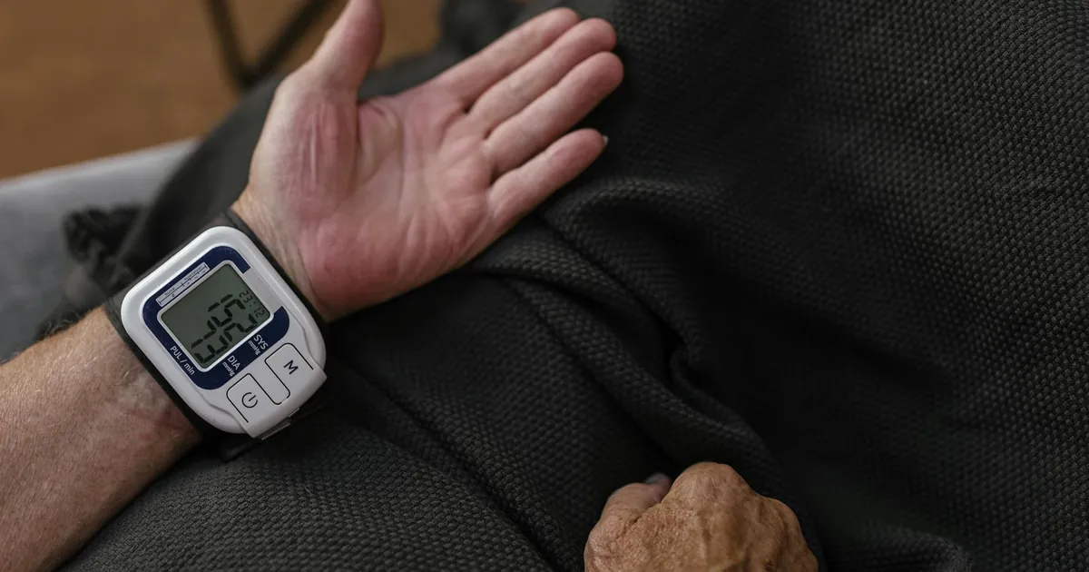 A senior adult using a wrist blood pressure monitor at home, focusing on health management. A senior adult using a wrist blood pressure monitor at home, focusing on health management.