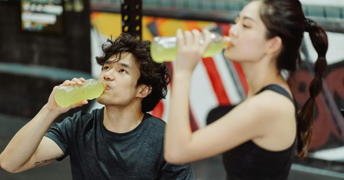 Fit Asian couple hydrating at the gym after an intense workout. Refreshing drink break.
