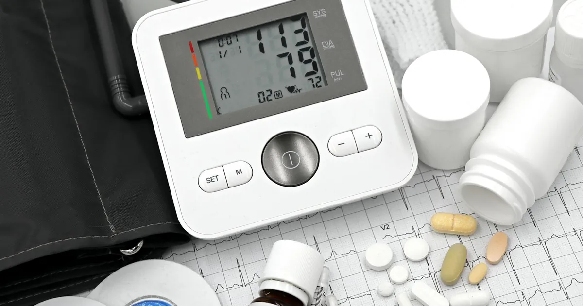 Digital blood pressure monitor on ECG paper with pills and medical supplies, ideal for healthcare topics.
