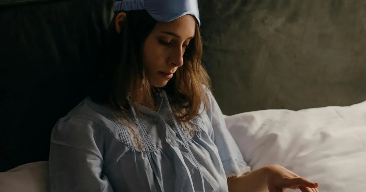 A woman in pajamas and sleep mask relaxing in bed, creating a cozy atmosphere. A woman in pajamas and sleep mask relaxing in bed, creating a cozy atmosphere.