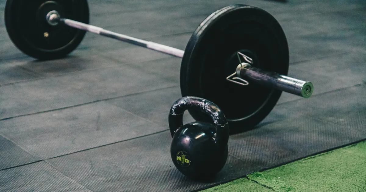 Barbell and kettlebell on gym floor, ideal for fitness and strength training themes.