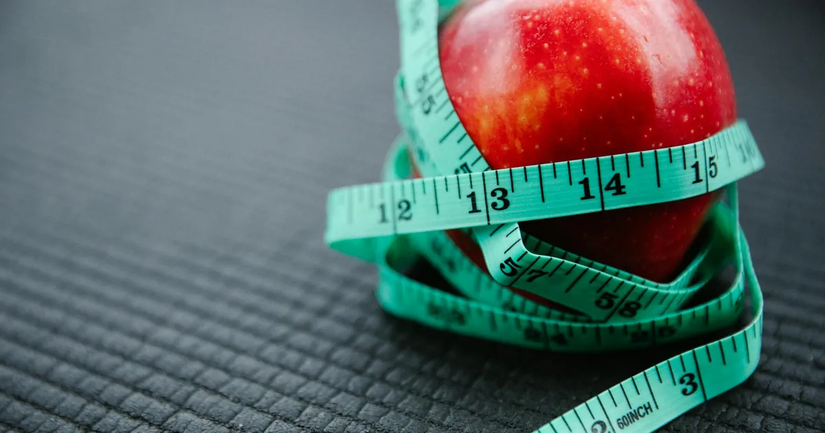 A vibrant red apple encircled by a blue measuring tape, symbolizing health and weight management.