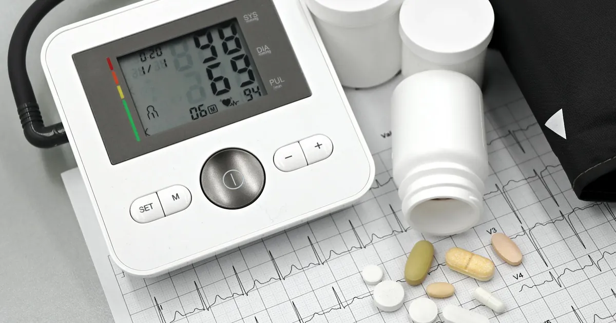 Blood pressure monitor with pills on ECG sheet, essential for heart health management. Blood pressure monitor with pills on ECG sheet, essential for heart health management.