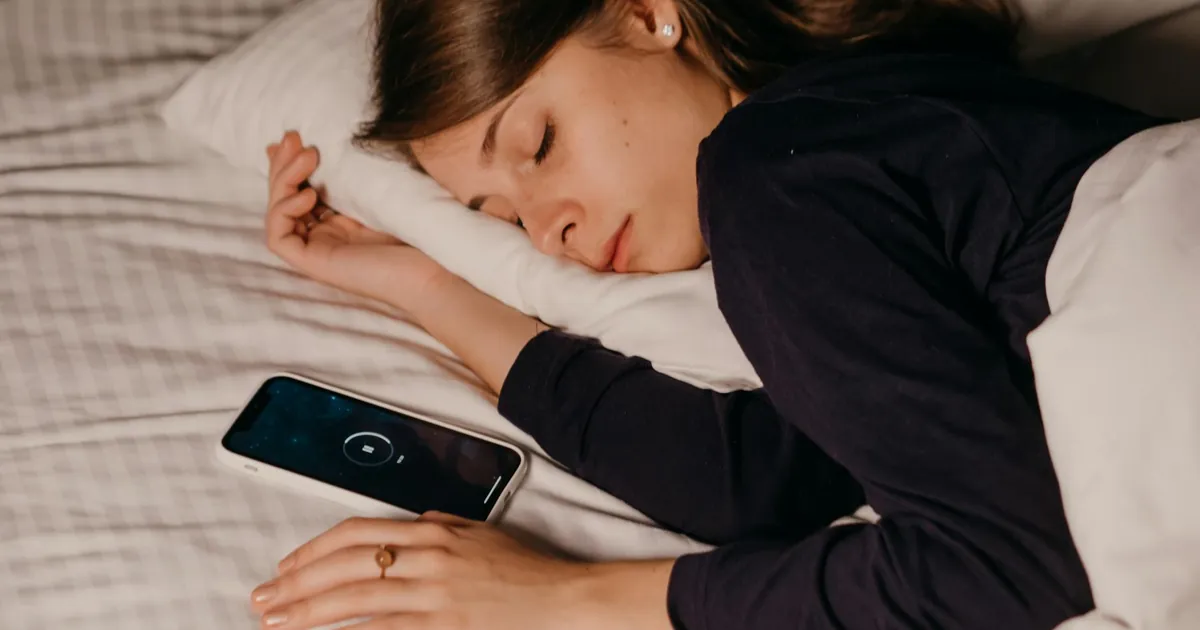 A woman peacefully sleeping in bed with a smartphone nearby, conveying rest and relaxation. A woman peacefully sleeping in bed with a smartphone nearby, conveying rest and relaxation.