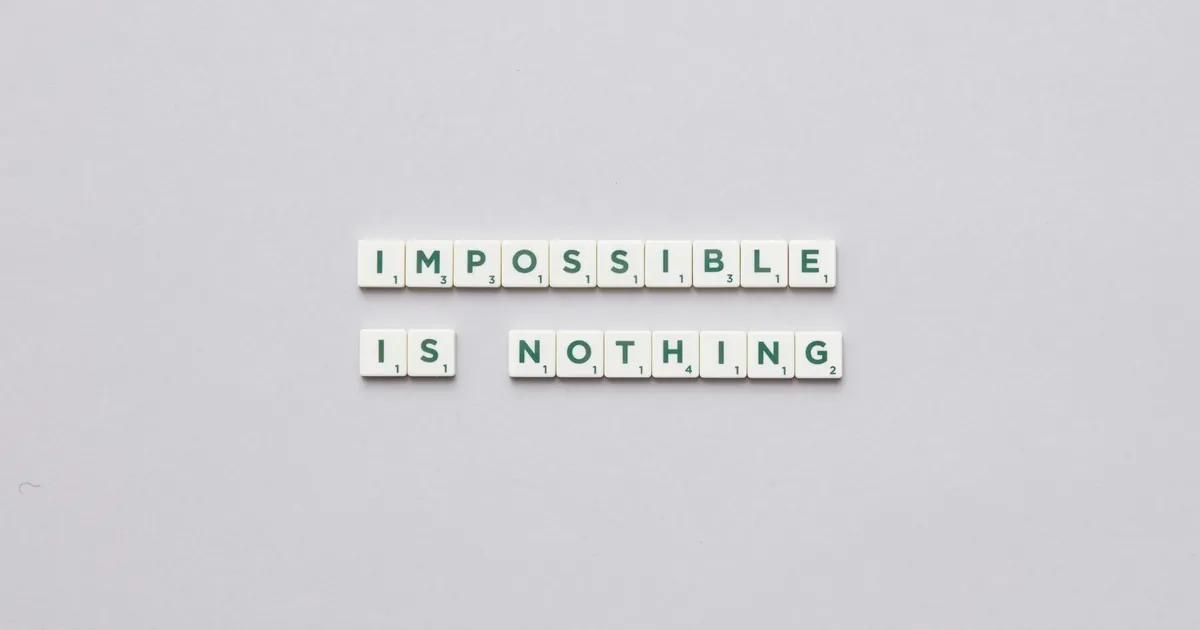 Flat lay of Scrabble tiles spelling 'Impossible is Nothing' on a neutral background.