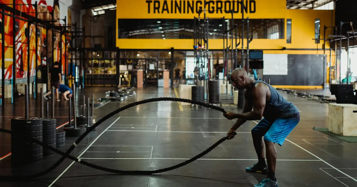 Athletic man engaging in a battle rope workout inside a modern gym setting for fitness training.
