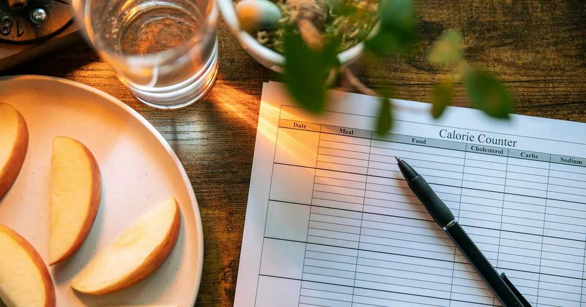 Apple slices, water glass, and a pen on a calorie counter sheet - a healthy lifestyle concept.
