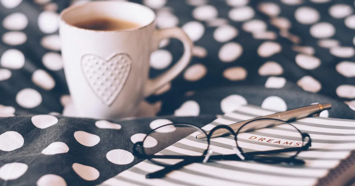 Relaxing morning scene with a hot coffee, dream journal, and eyeglasses on a stylish polka dot bedspread. Relaxing morning scene with a hot coffee, dream journal, and eyeglasses on a stylish polka dot bedspread.
