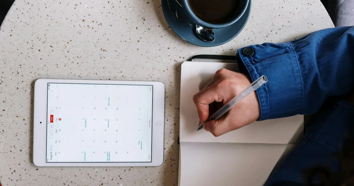 Overhead view of planning with a tablet, notebook, and coffee on a table.