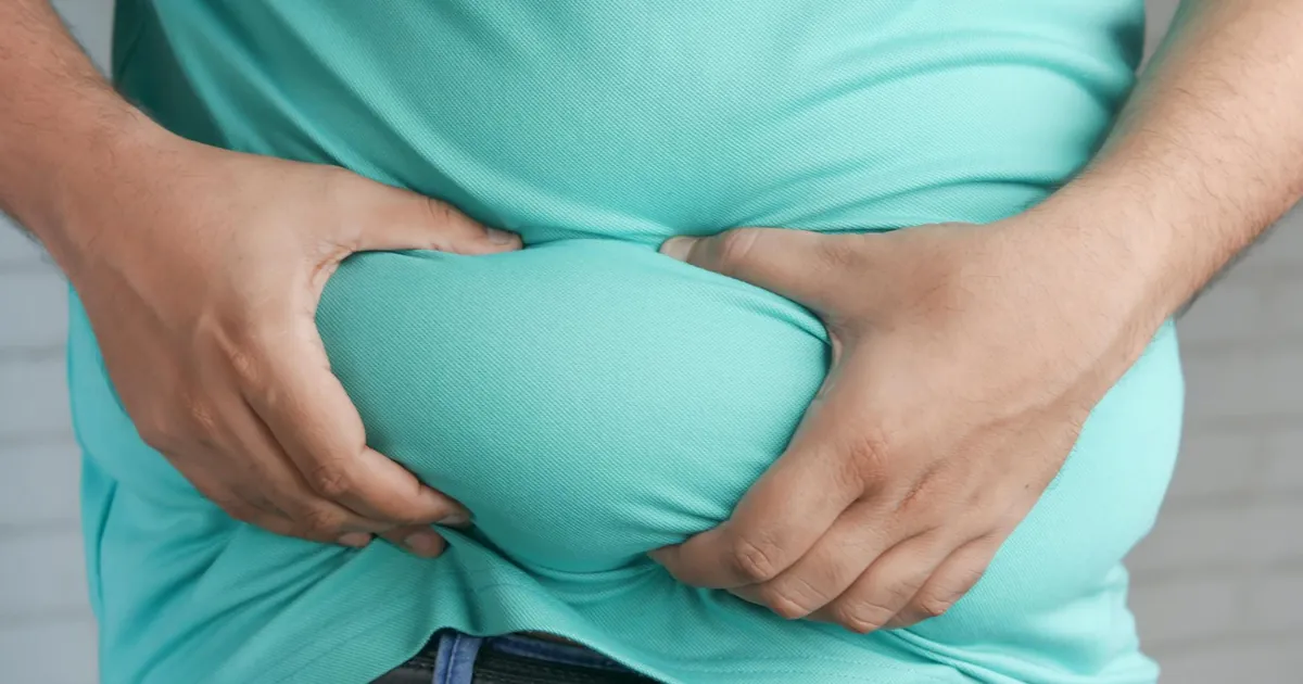 Close-up of hands gripping an overweight belly, depicting body fat focus.