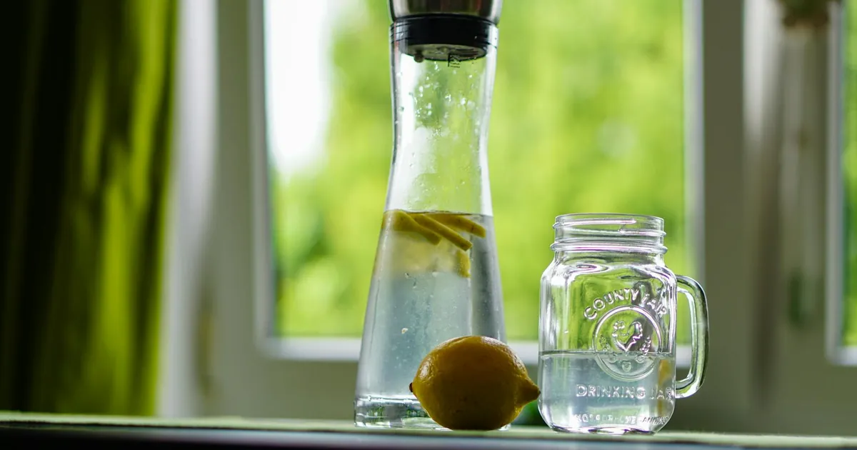 Lemon-infused water in a glass carafe and mason jar on a windowsill, evoking freshness.