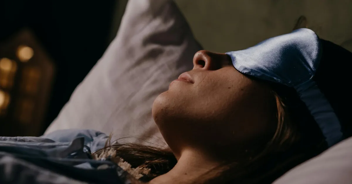 A serene scene of a woman wearing a blue eye mask, sleeping soundly in a cozy indoors setting. A serene scene of a woman wearing a blue eye mask, sleeping soundly in a cozy indoors setting.