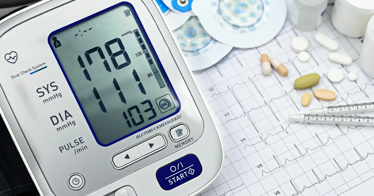 Close-up of a digital blood pressure monitor with ECG printout, pills, and medical tools. Close-up of a digital blood pressure monitor with ECG printout, pills, and medical tools.