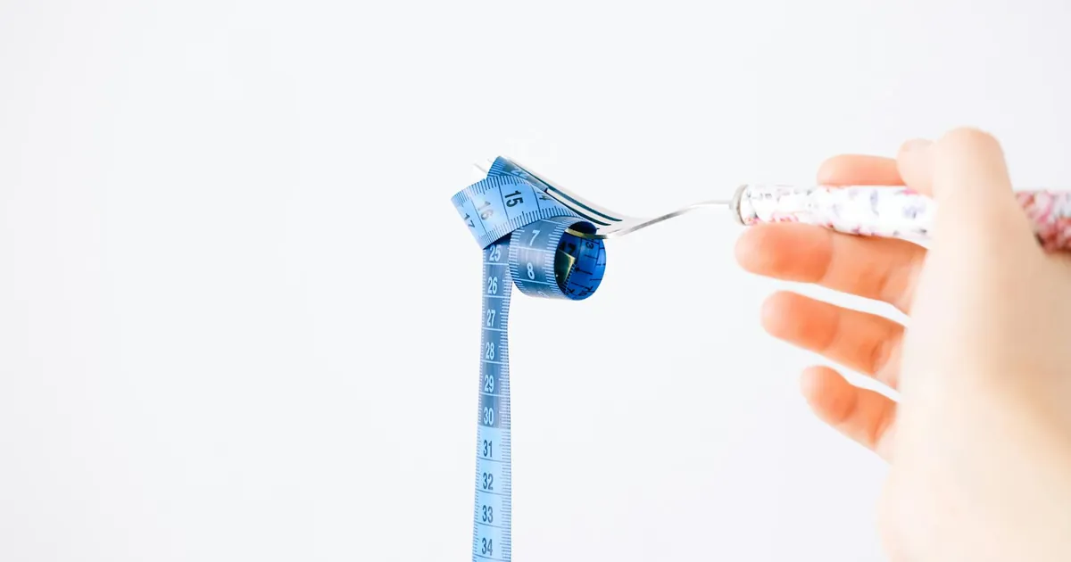 A blue measuring tape wrapped around a fork representing dieting or healthy eating concept.
