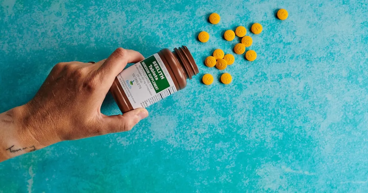 a hand holding a bottle of pills on a blue surface a hand holding a bottle of pills on a blue surface