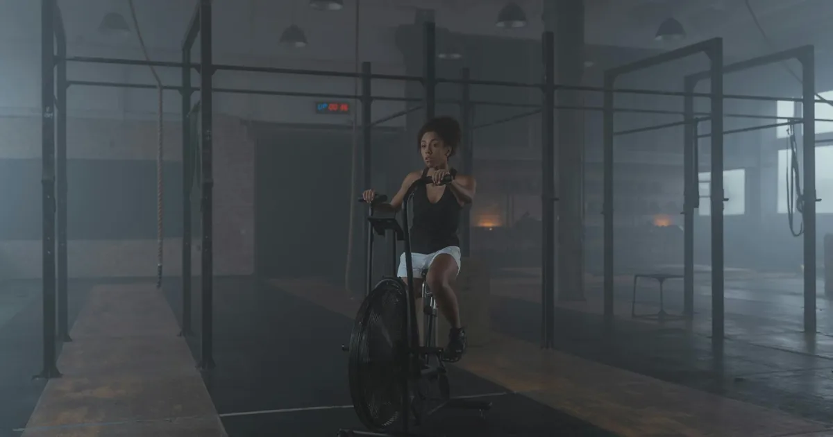 A woman works out on a stationary bike in a dimly lit gym setting, promoting fitness and healthy living.