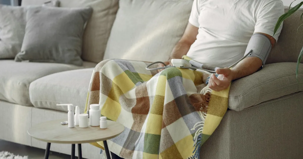 Elderly man monitoring blood pressure on a cozy couch at home, surrounded by medication. Elderly man monitoring blood pressure on a cozy couch at home, surrounded by medication.