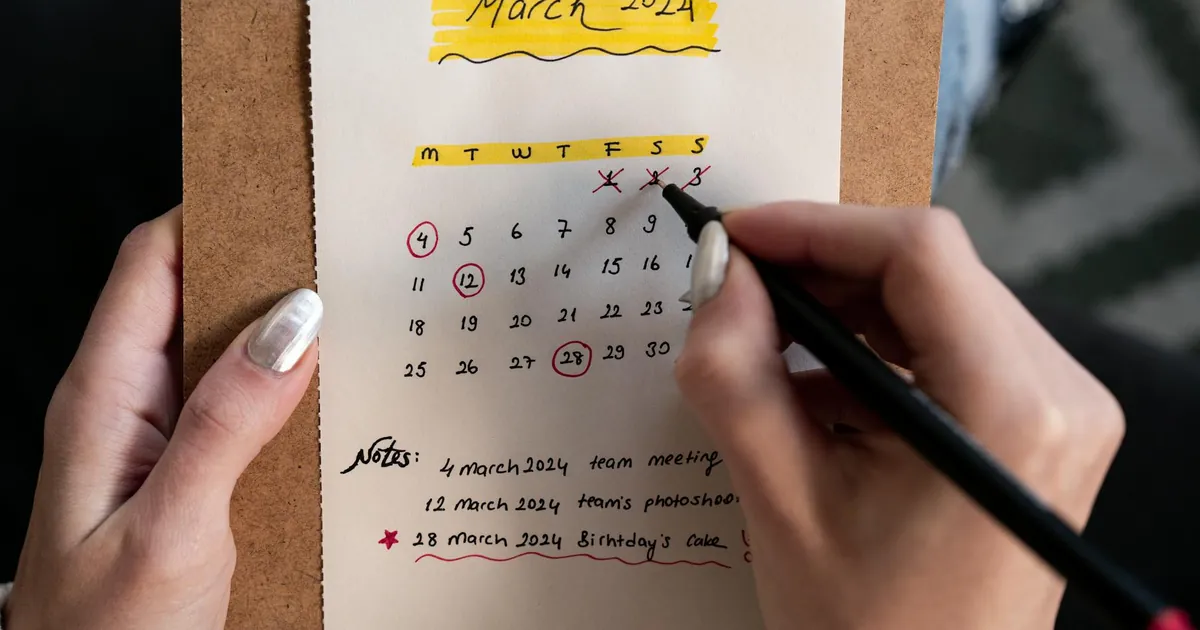 Close-up of a woman's hands organizing a planner for March 2024 with handwritten notes and highlights.
