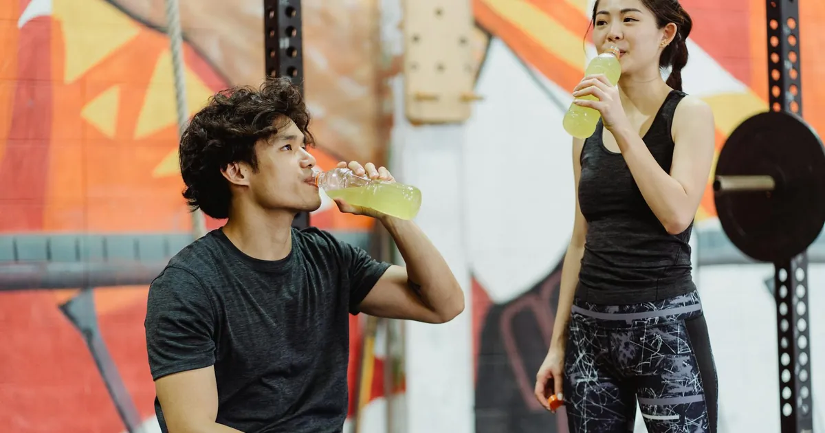 Asian couple in gym attire drinking energy drinks after workout. Vibrant and lively setting.