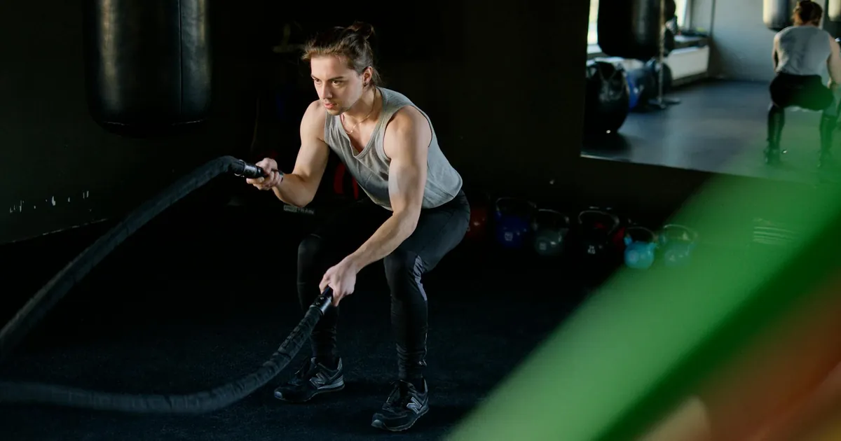 Man engages in an intense battle rope workout in a gym, focusing on fitness and strength.